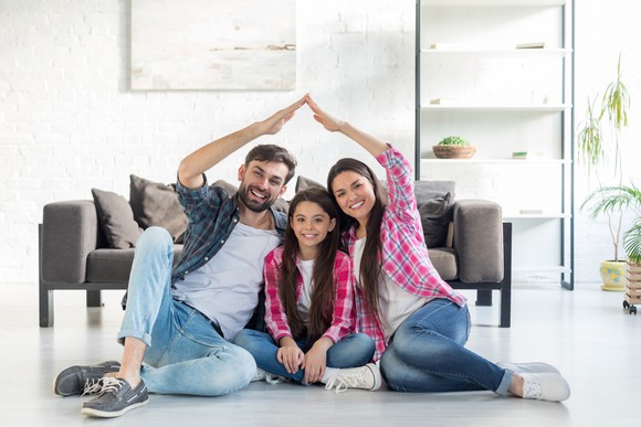 Young parents making a house over their daughter's head with their hands.
