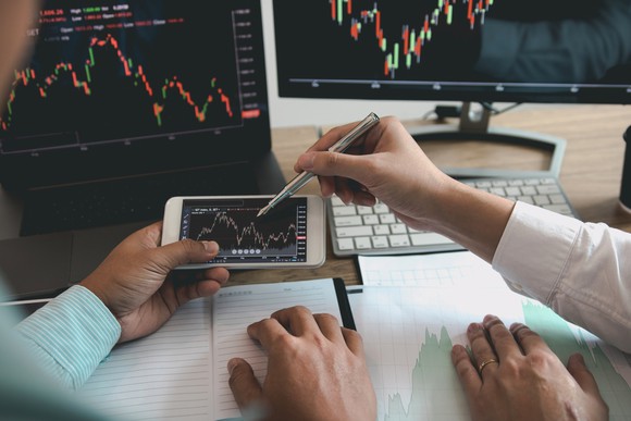 Two people pointing at stock charts.