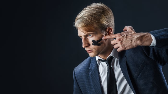 A man in a business suit putting black paint under his eyes.