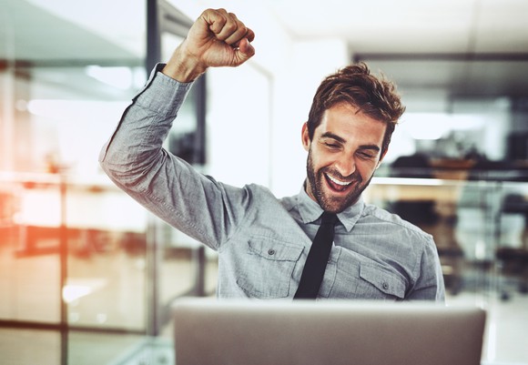 Smiling man at laptop raising arm in victory