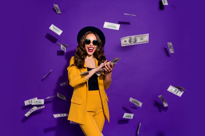 Fashionably dressed young lady throwing $100 bills in the air against a purple background