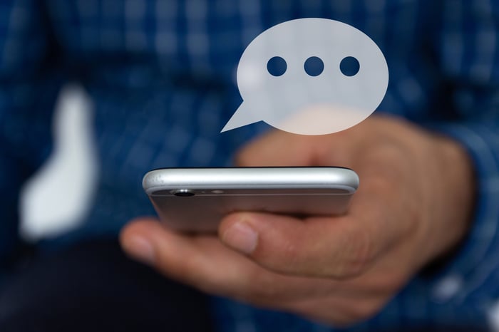 A person texting on their smartphone, with a chat bubble appearing above their device. 