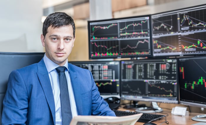 A man sitting in front of computer screens with stock information on them.