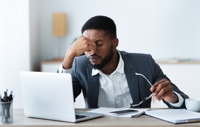 Frustrated investor with head in hand and an open laptop.