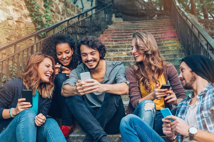 A group of young adults sitting on stairs outside looking at their cellphones.