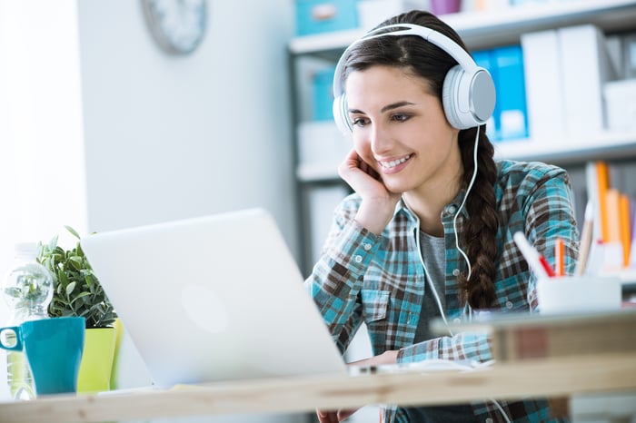 A young woman wearing headphones while looking at her open laptop.