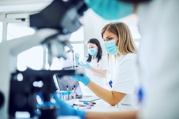 Gloved and masked medical researchers using microscopes in their work.