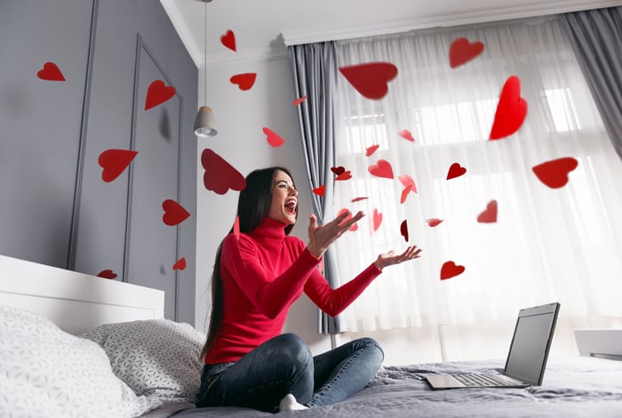 Woman sitting on bed with laptop and swirling hearts