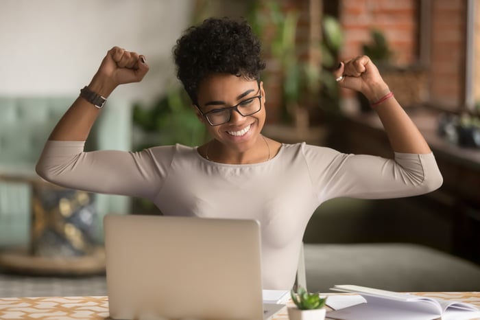 A woman raising her arms in triumph in front of a computer.