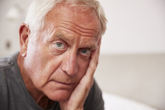 Closeup of older man with serious expression resting face on hand