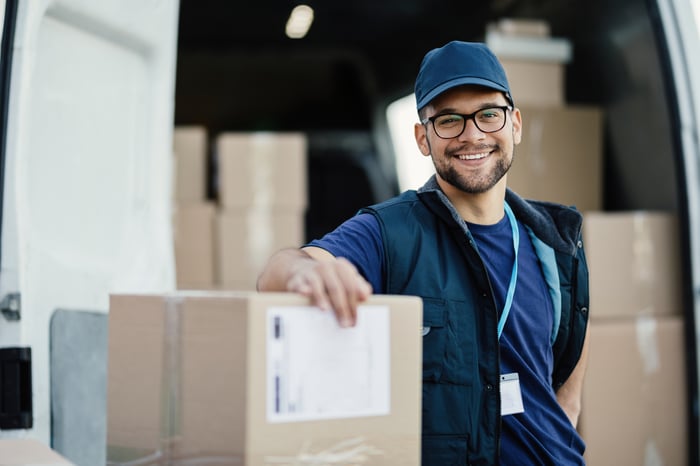 A delivery man with a package standing next to a delivery van.