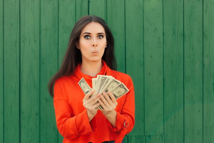 A woman holding a fan of singles making a wow face.