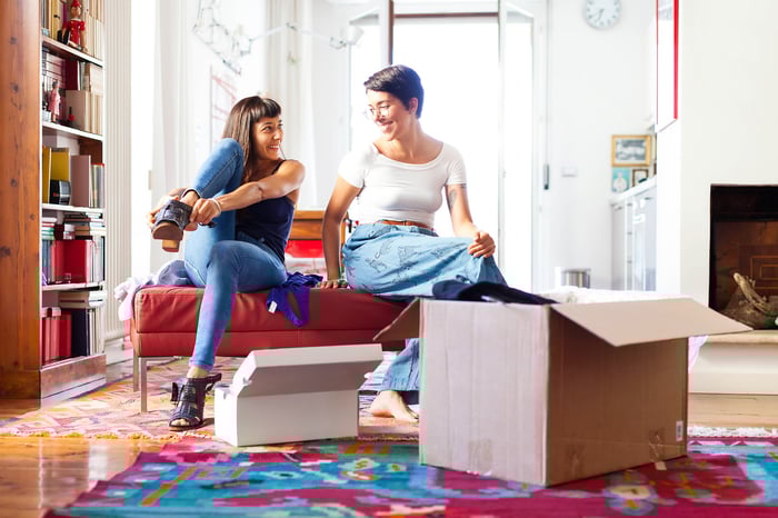 Two women try on clothing and accessories taken from delivery boxes