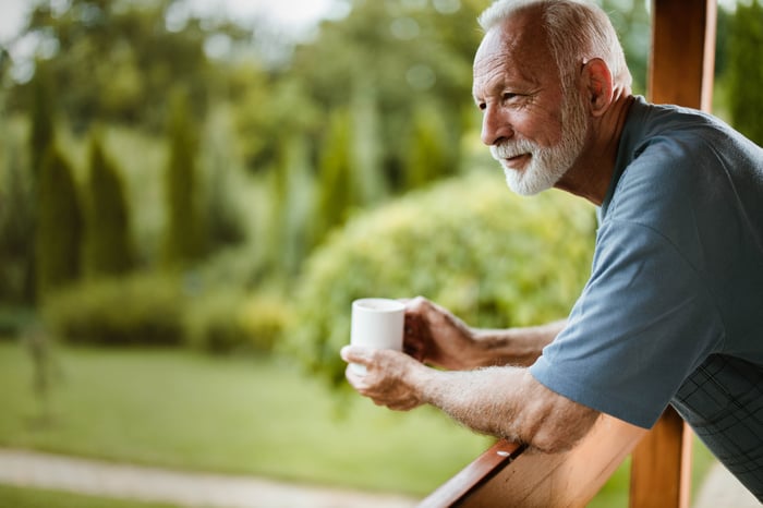 Smiling older man holding mug outdoors while leaning on railing