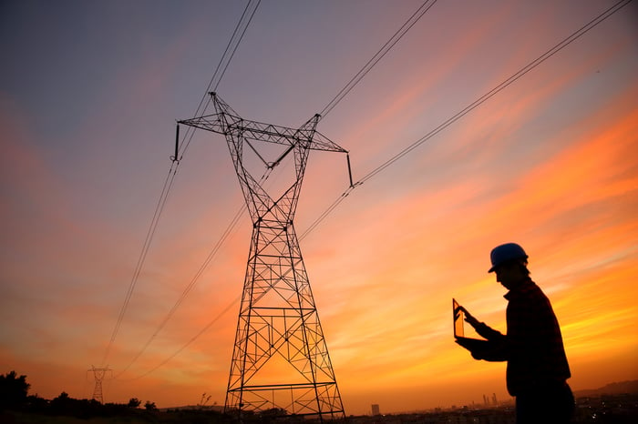 An engineer works in front of a high voltage tower at sunrise.