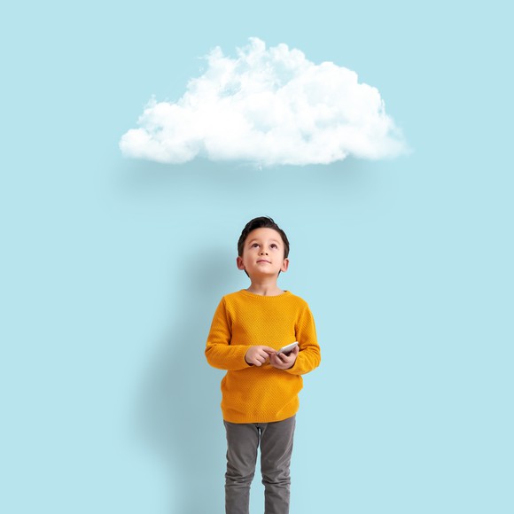 Little boy holding a device while staring at a cloud above him.