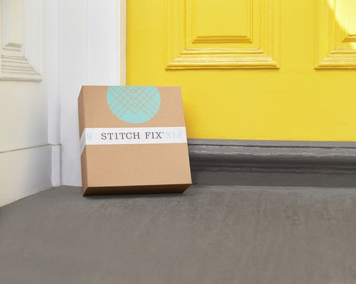 Close-up of a Stitch Fix package leaning against a bright yellow door surrounded by white trim. 