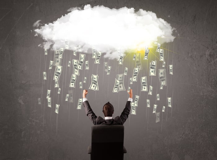 Business man in suit looking at cloud with falling $100 bills.