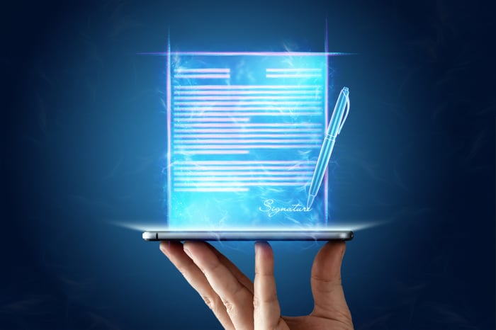 Fingers balancing a mobile device with an e-signature icon projected above the device.