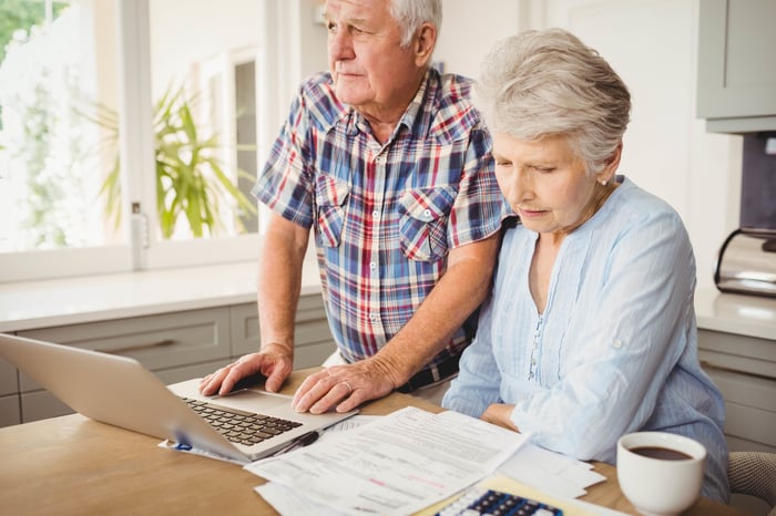 Older man and woman with concerned expressions at laptop with papers next to it