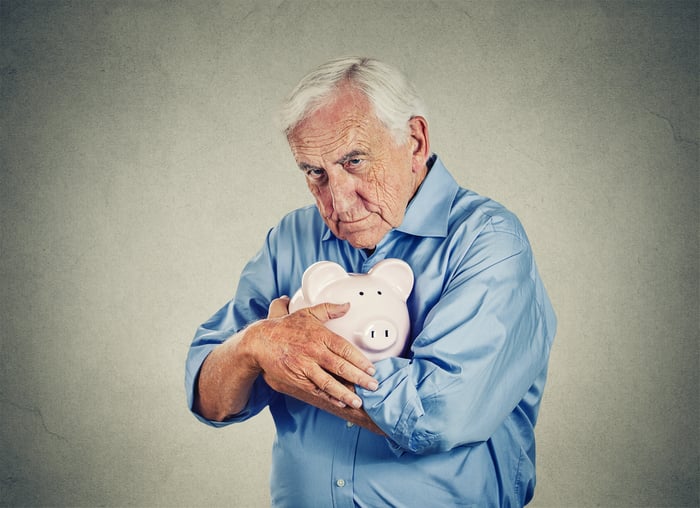 Senior man holding a piggy bank tightly