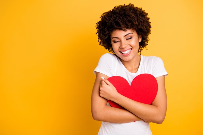 A young woman is hugging a red heart cutout and smiling.