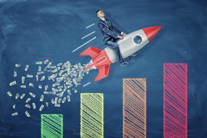 A businessman rides a rocket ship expelling cash exhaust over a multi-colored bar chart.