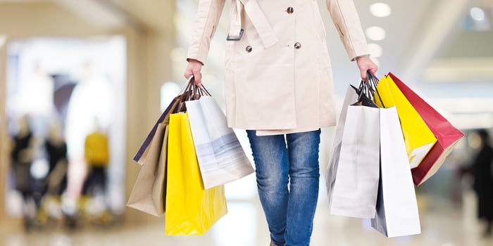 A woman carrying multiple shopping bags in each hand inside in a mall. 