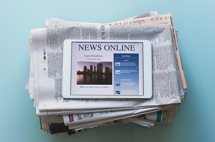 tablet with news online sitting on stack of newspapers