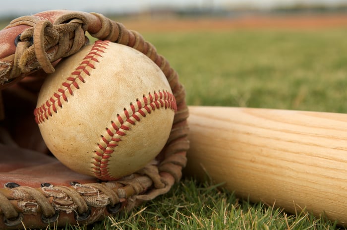 A baseball resting in a baseball mitt next to a bat in the grass.