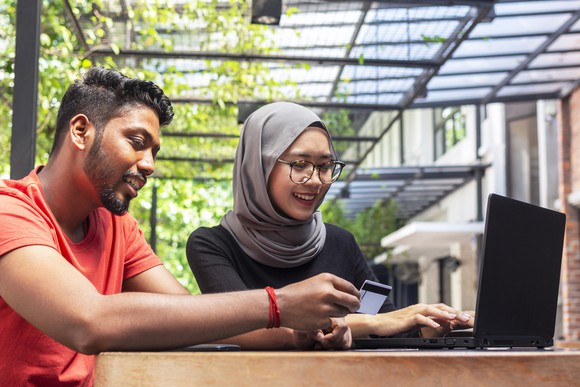 A man and a woman using a laptop as the man holds a credit card.