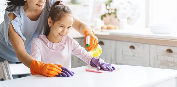 A mother and child clean a countertop together.
