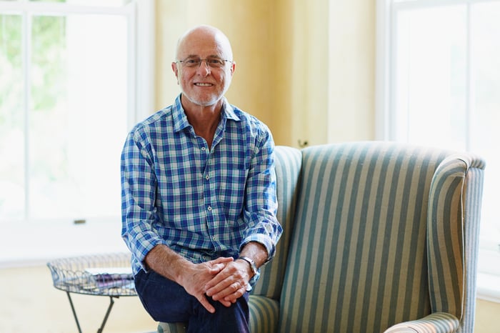 Smiling older man perched on edge of chair