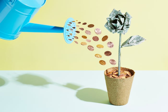 A rendering of a watering can shooting coins into a plant that sprouts a flower made of cash. 