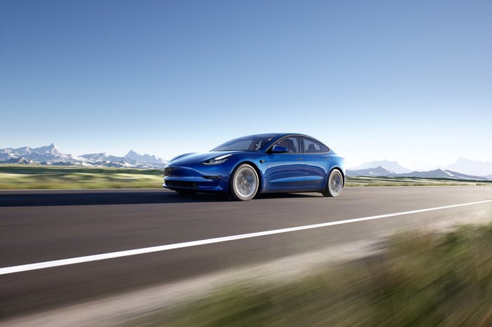 Tesla Model 3 speeding down road with snowy mountains in the background.