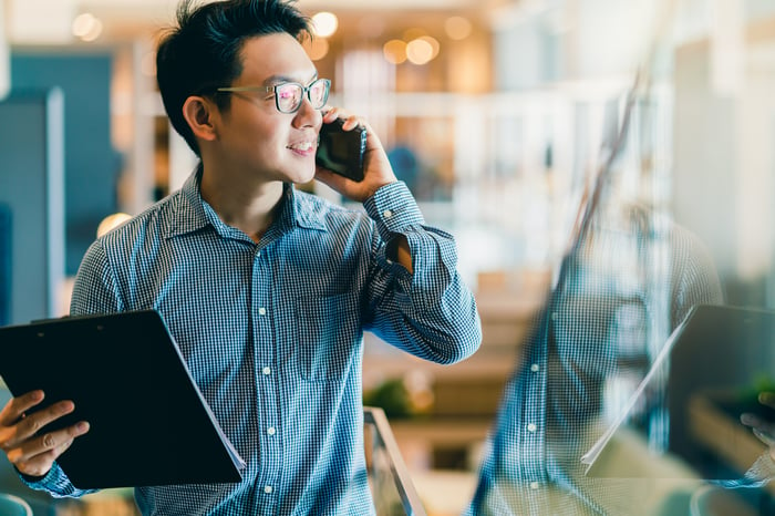 A man uses a cell phone while holding documents.