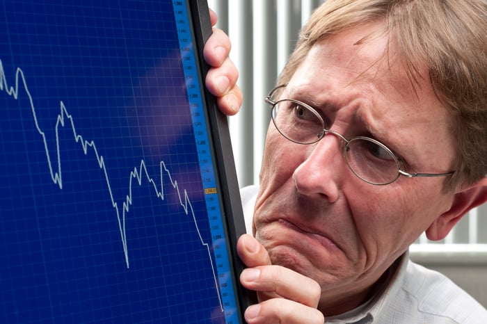 A visibly worried man looking at a plunging chart on a computer monitor.