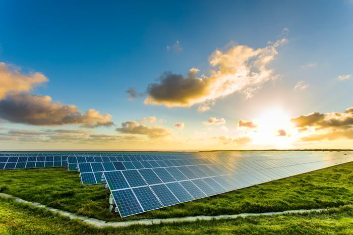 The sun rises over rows of solar panels in a field.