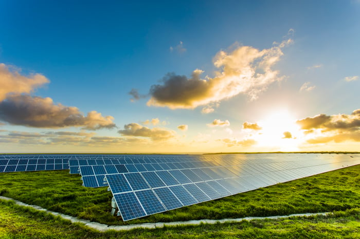 The sun rises over rows of solar panels in a field.