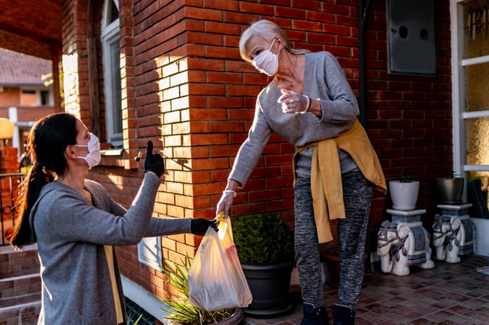 A masked woman delivers groceries to an elderly woman's home.