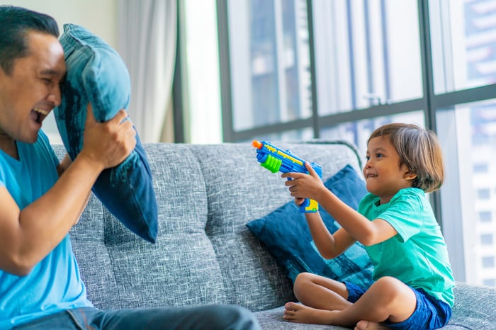 Little boy playing with a toy gun on a couch with his dad