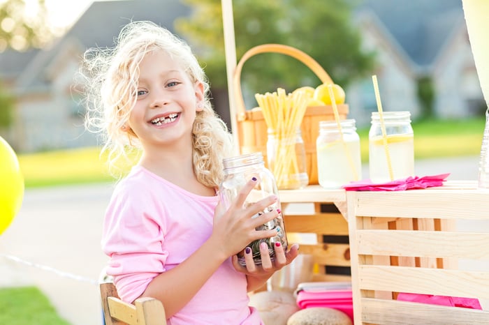 A girl with a lemonade stand holding a jar of coins.