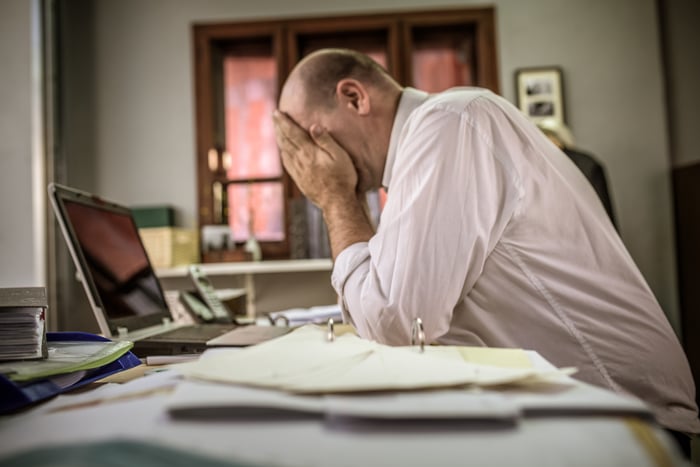 Upset man covering his face while sitting at a laptop