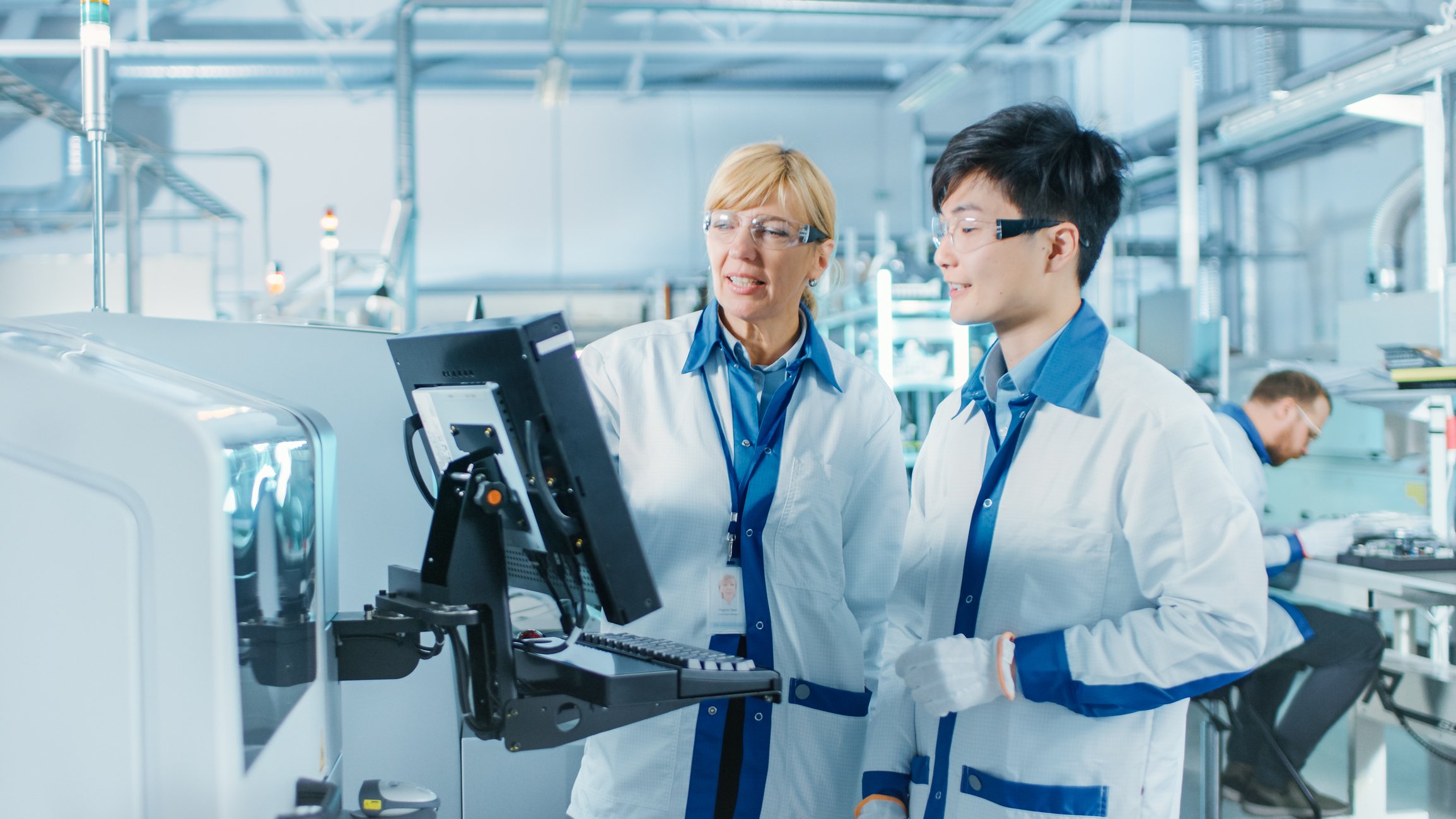 two pharmaceutical manufacturing employees look at a computer together