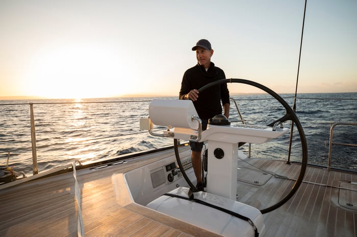 An older man at the steering wheel of a large boat.