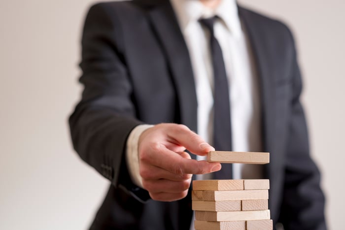 A business person strategically placing wooden blocks on a block tower.