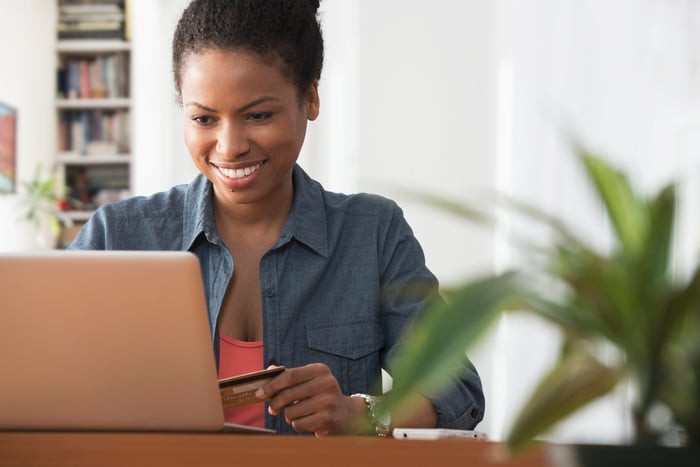 A woman holding a credit card in her left hand, while preparing to make an online purchase.