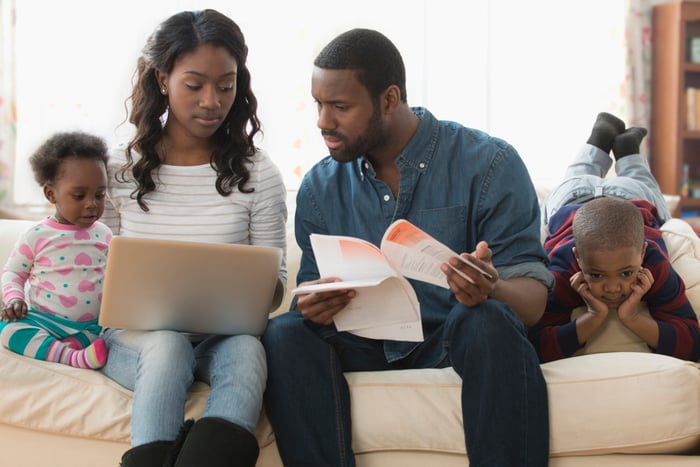 Stressed couple with two kids holding papers and looking at laptop