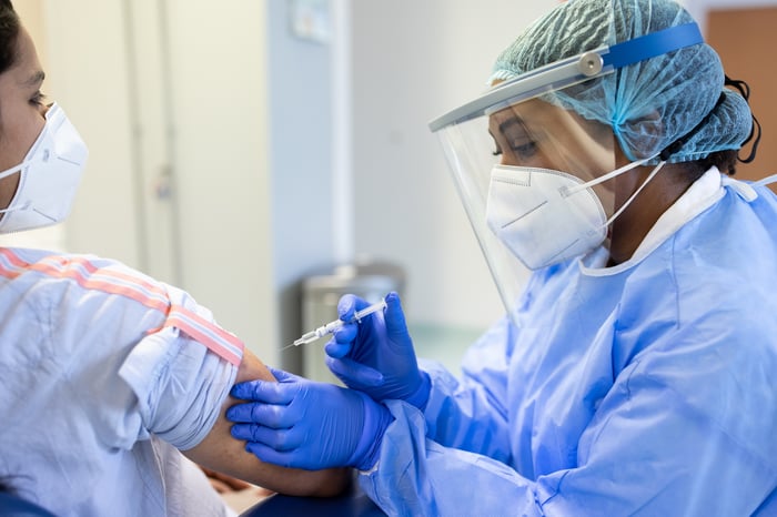 Doctor administers a vaccine to a patient while wearing full personal protective equipment.