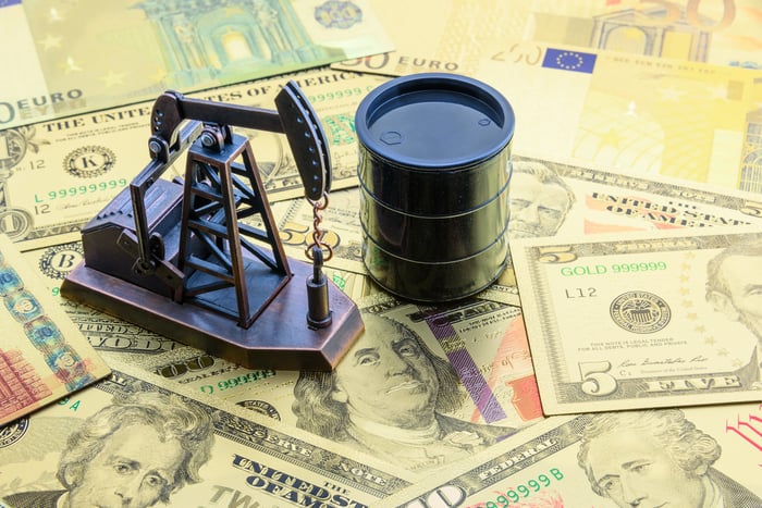 Toy oil rig and barrel atop various denominations of currency.